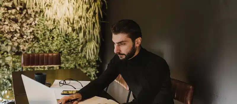 Businessman working on laptop in a stylish indoors office with greenery wall and sleek furniture.