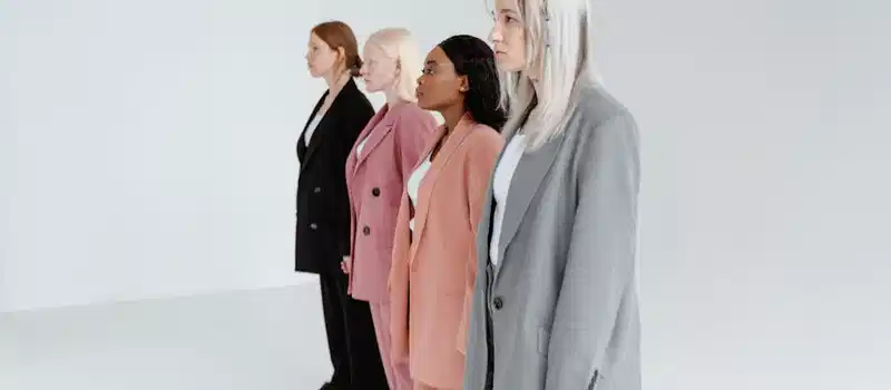 A group of diverse women wearing fashionable business suits in a minimalist studio setting.