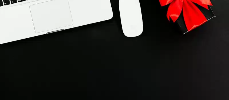 Flat lay of laptop and gift box with red bow on black background. Ideal for online shopping or gift themes.