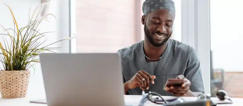 Smiling healthcare professional using phone in office with laptop and medical tools.