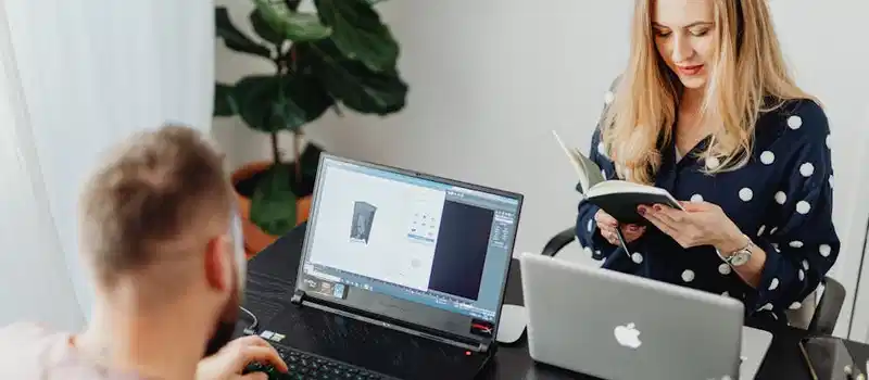 Professional coworkers collaborating in a modern office setting with laptops and a notebook.