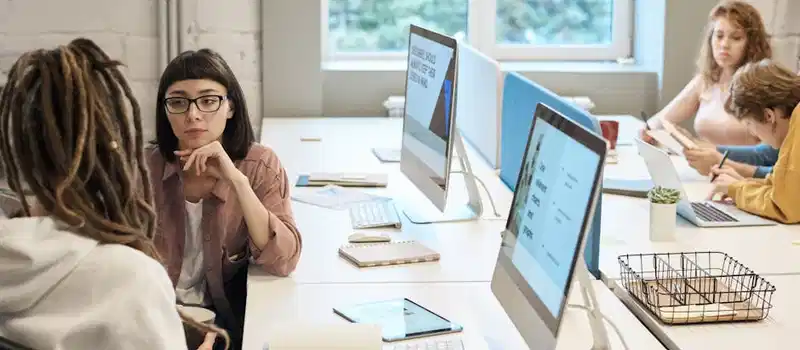 Diverse group of women working together in a modern office setting, fostering teamwork and creativity.