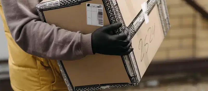 Courier holding a package marked 'TOP PACKAGING' wearing gloves for safe delivery.