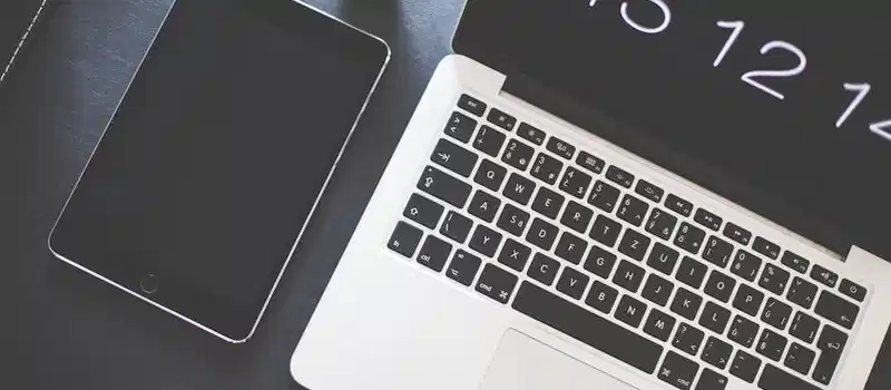 Top view of a stylish workspace featuring a laptop, tablet, and sunglasses.