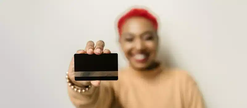 Close-up of a credit card held by a smiling person, emphasizing modern finance and personal identity.