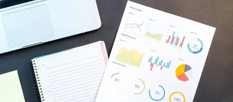 Flatlay of business report with colorful charts, a notebook, and a laptop for data analysis on a desk.