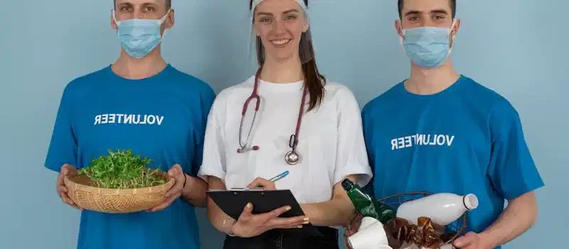 Three volunteers promoting eco-friendly practices with plants and recycling materials.