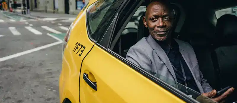 Happy confident mature African American male looking away and expecting important message on mobile phone while sitting in yellow automobile