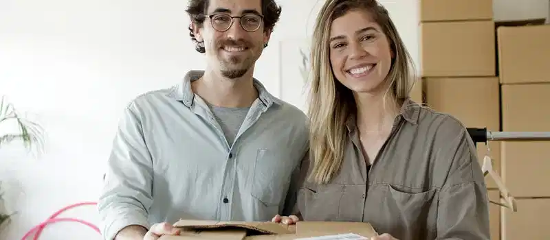 Happy business partners holding a package in a startup office with stacked boxes. Ideal for small business themes.