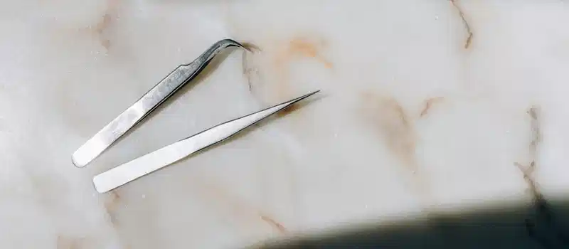 High-angle shot of two precision tweezers on a marble surface, highlighting elegance and simplicity.