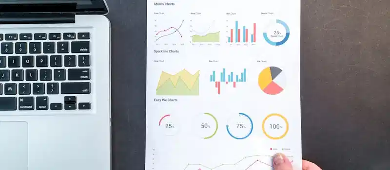 Detailed charts and graphs on a document next to a laptop, representing data analysis.