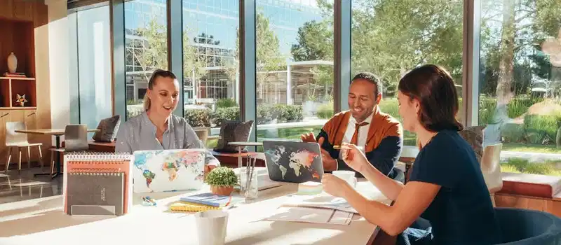 Three colleagues brainstorming with laptops in a well-lit office.