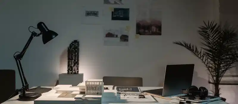 A contemporary architect's desk with design plans, laptop, and lamp in a spacious office.