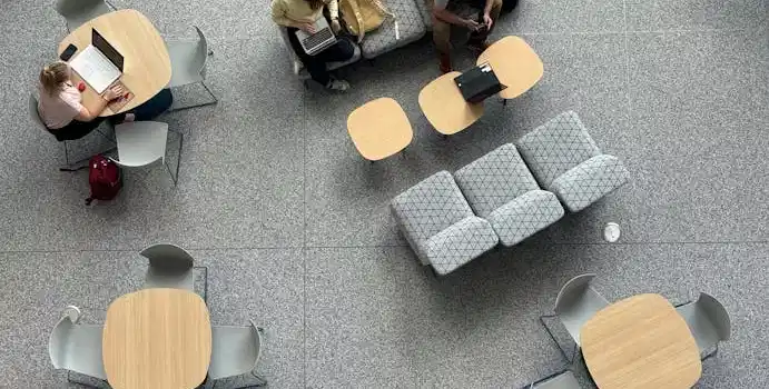 Aerial view of people working at modern tables with laptops in a spacious hall.