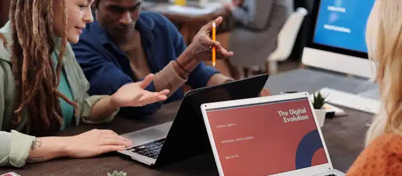 Diverse team collaborating with laptops in a modern office setting, discussing digital evolution.