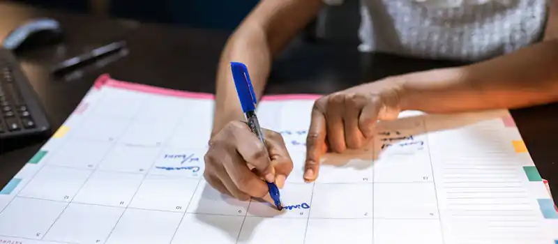 A woman marks important dates on her desk calendar, planning upcoming events.
