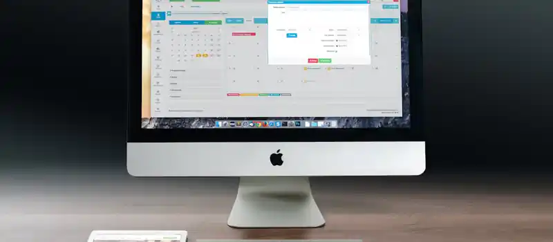 A sleek office setup featuring an Apple iMac, iPad, and keyboard on a wooden desk.