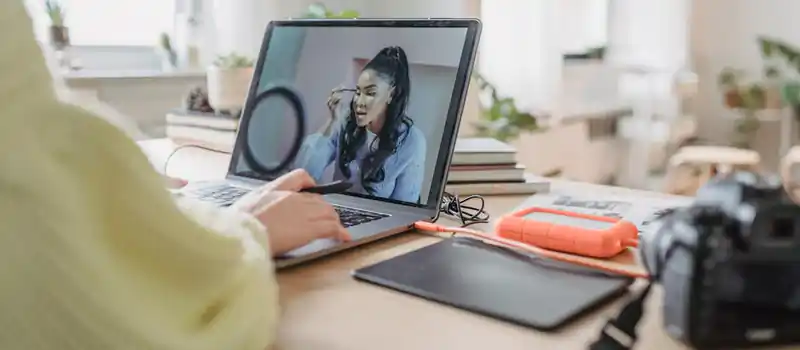 Crop unrecognizable female photographer editing photo while sitting at table with photo camera and graphic tablet during work in spacious room with flowerpots