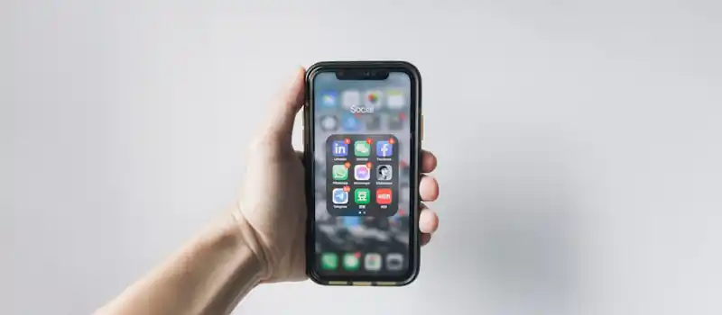 Hand holding smartphone displaying social media apps on home screen.