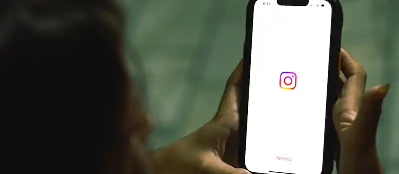 Close-up of a woman holding a smartphone displaying the Instagram app indoors.