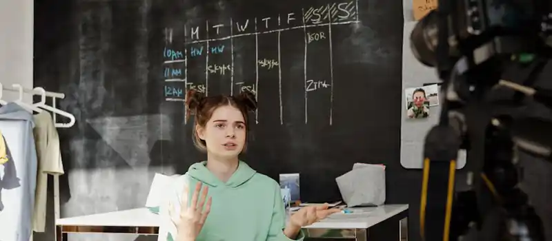 Teen girl in hoodie talking in front of camera for a vlog indoors, showcasing vlogging setup.