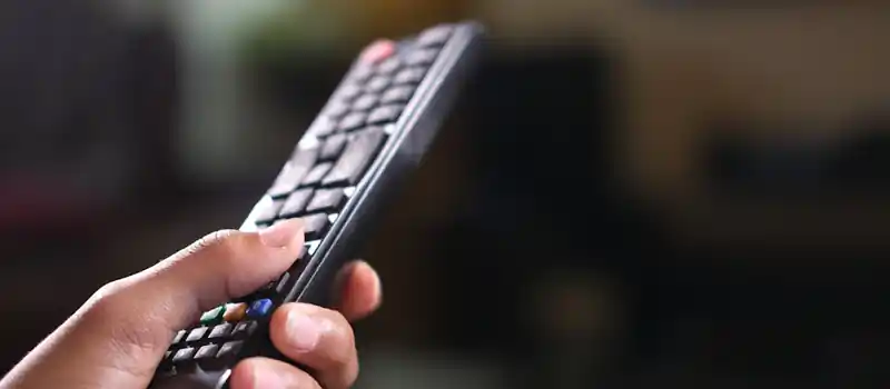 Hand holding a TV remote control, focusing on buttons and grip indoors.
