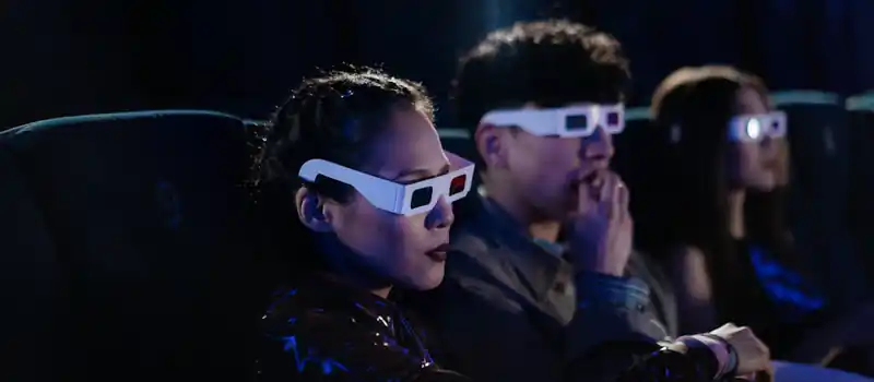 Friends enjoying a 3D movie night at the cinema, wearing glasses and eating popcorn.