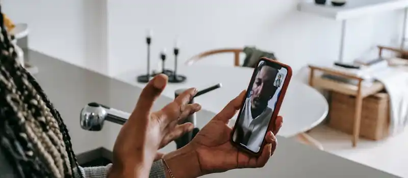 High angle of crop unrecognizable young black female gesticulating while having video conversation on smartphone with boyfriend in kitchen