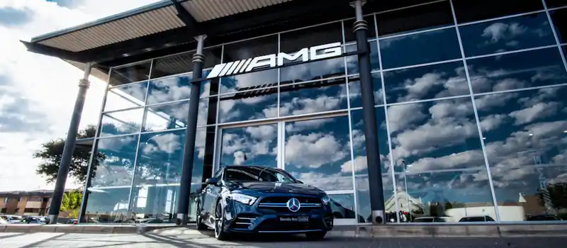 A sleek blue Mercedes-Benz parked outside the AMG showroom reflecting a cloudy sky.