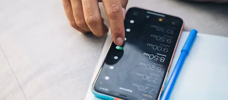 Close-up of a hand touching a smartphone with a blue case and a pen nearby.