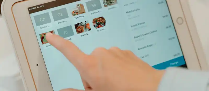 Finger tapping on a tablet screen to select food items in a restaurant setting.