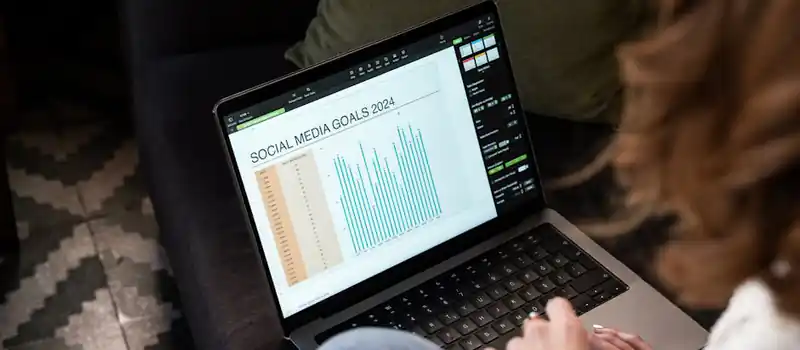 A woman reviewing 2024 social media goals on a laptop at home.