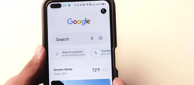 A close-up of a hand holding a smartphone with Google search displayed on the screen.