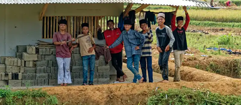 A cheerful group of boys posing near a rural structure in Indonesian farmland.