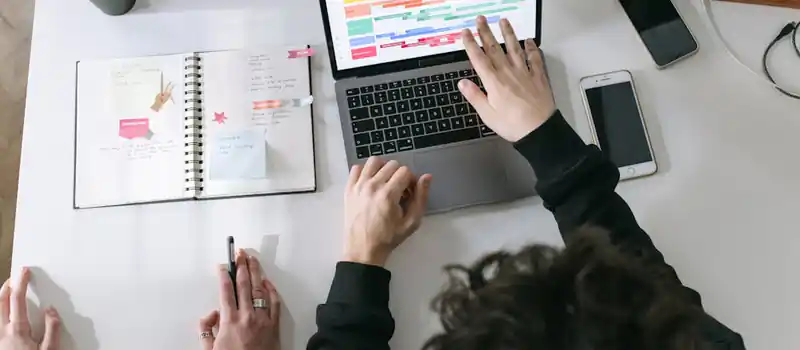 Two people collaborating on a laptop and planner at a vibrant modern office desk.