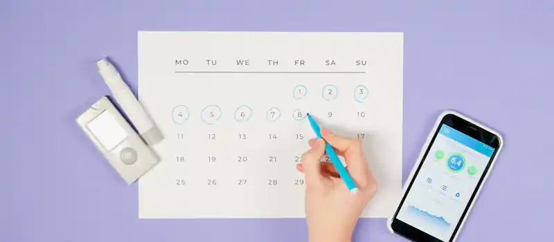 Hand marking days on a calendar with glucose monitor and smartphone app, emphasizing diabetes management.