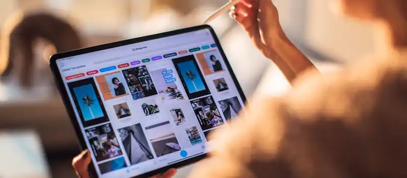 A person uses a digital tablet with a stylus indoors in a warm, cozy setting.