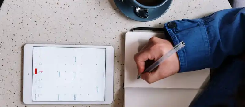 Overhead view of planning with a tablet, notebook, and coffee on a table.