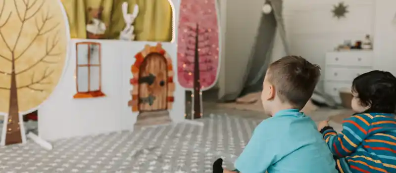 Two children watching a charming indoor puppet show with colorful backdrop.