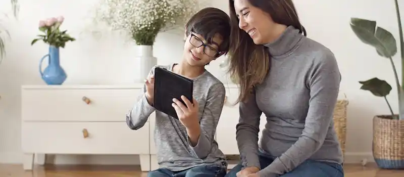 A mother and son enjoying time together with a tablet indoors, showcasing family bonding.