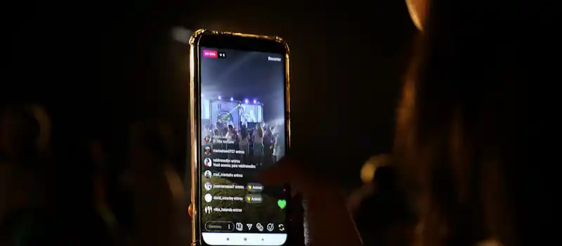 A woman live streams a concert using her smartphone at night. Vibrant stage in view.