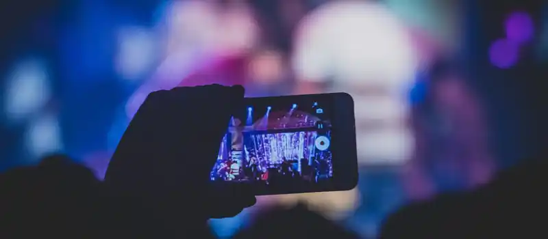 A hand holds a smartphone recording a live concert with vibrant lights.