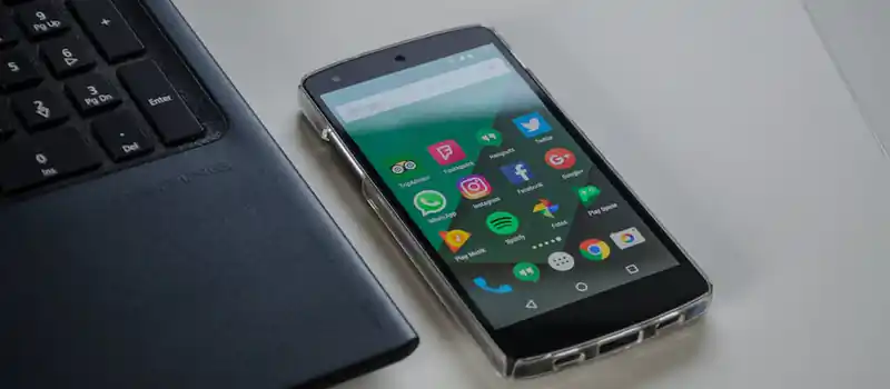 Smartphone on a table showing various social media apps beside a laptop keyboard.