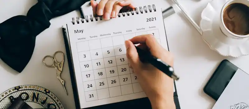 Top view of hands using a planner with coffee and accessories, focused on May 2021 calendar.