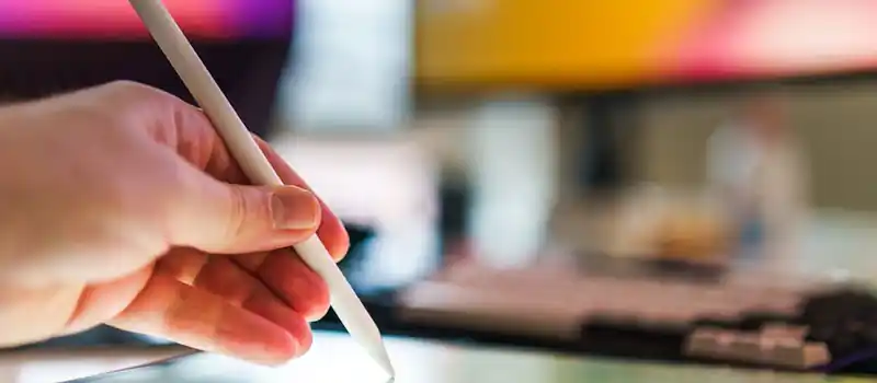 Close-up of a hand using a stylus on a digital tablet in a creative workspace.