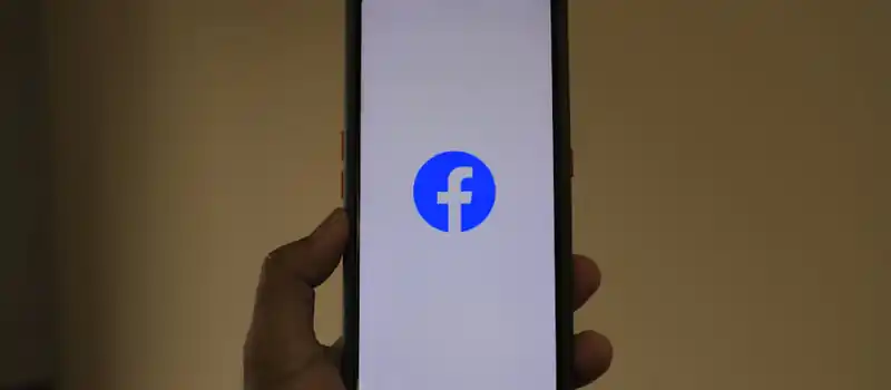 A smartphone held in hand showing the Facebook logo on its screen.