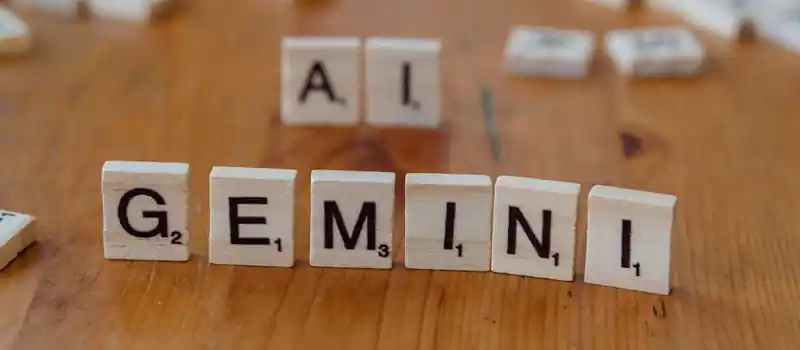 Scrabble tiles spell out the words 'Gemini' and 'AI' on a wooden surface, symbolizing technology and communication.