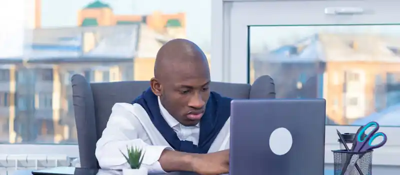 Adult male focused on work at his desk with a laptop in a modern office setting.