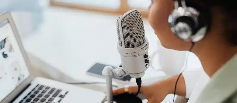 Professional woman recording a podcast or broadcast using a microphone and laptop at a desk.