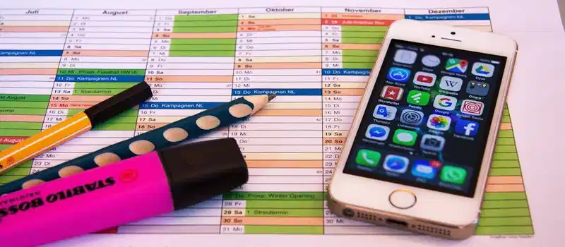A desk setup featuring a planner, pens, and a smartphone displaying app icons, ideal for productivity.